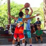 Programs 10 1. Young basketball players competing in an outdoor game amidst lush greenery.