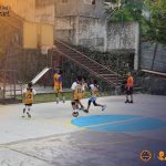Programs 13 Playing basketball on an outdoor court in Subic Bay, with children and a coach, surrounded by urban.