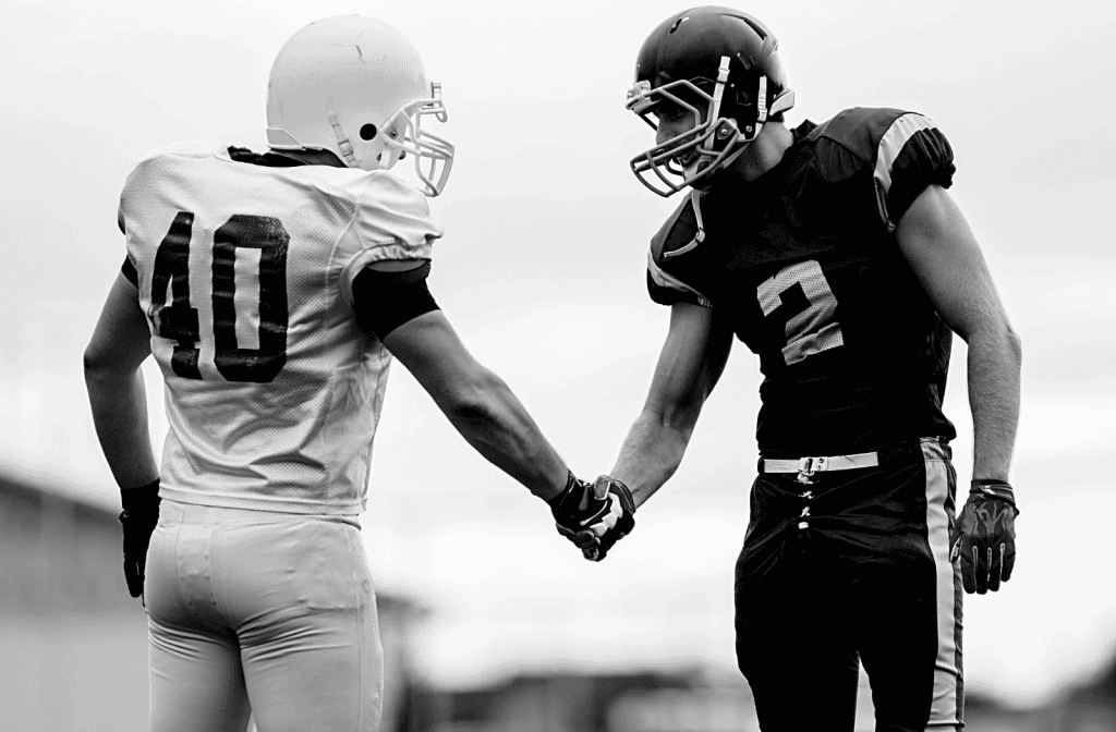 Two football players shaking hands on the field before a game.